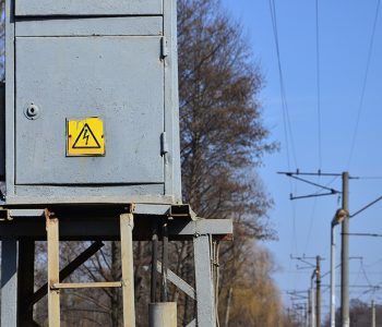 Electrical transformer in gray with a symbol warning of the danger of high voltage near the railway line. A small substation for the supply of electricity